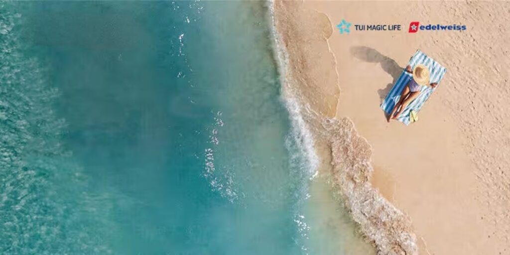 Frau entspannt auf blau-weiss gestreiftem Strandtuch am türkisfarbenen Meer, TUI Magic Life und Edelweiss Gewinnspiel