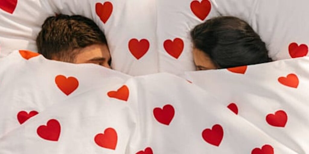Pärchen unter der Bettdecke mit roten Herzen