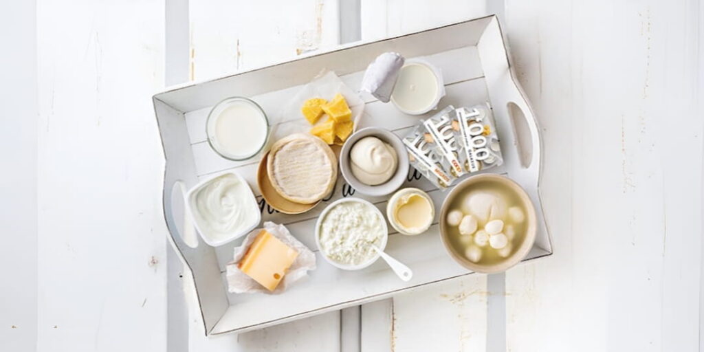 Milch-Quiz Wettbewerb – verschiedene Milchprodukte wie Milch, Joghurt, Käse, Mozzarella, Butter und Rahm auf weissem Holztablett mit Geschenkkarten von Galaxus, Migros und Coop als Preise zu gewinnen