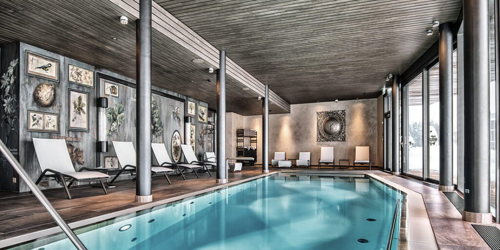 Indoor-Wellnesspool im Valsana Hotel Arosa mit Liegestühlen und alpiner Atmosphäre